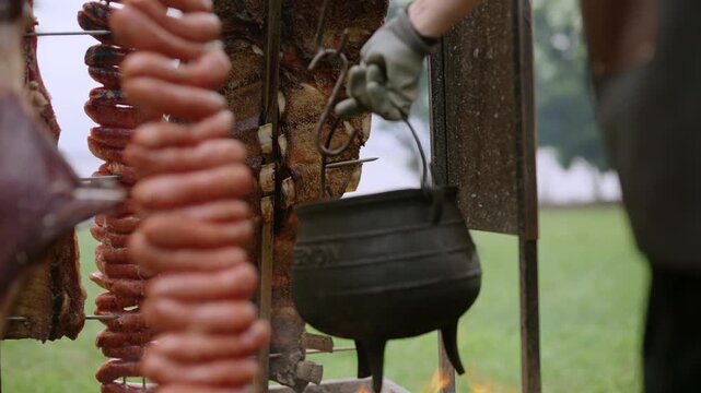 Traditional Argentine asado showing meat grilling over open coals and flames outdoors, pot added at center