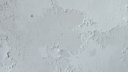 Abstract texture of an old white wall with widespread, rough, and heavily flaking paint, showing decay.