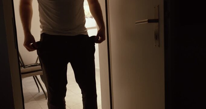 A man stands in a doorway showing his empty pockets. Symbol of financial struggle, debt, poverty, fear of the future, or middle-class crisis.