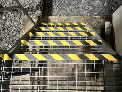 Metal grating staircase steps feature prominent yellow and black diagonal anti slip safety tape