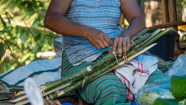 Assamese tribal woman preparing edible tender shoots of cane sticks for sale