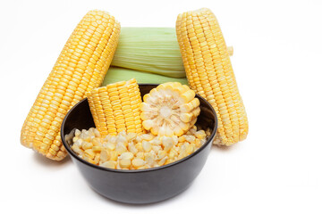 Black bowl with corn pieces and loose kernels, fresh corn cobs in the background