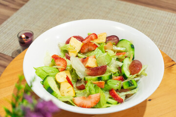 Photograph of homemade fruit and vegetable salad placed on a white plate on a wooden plate