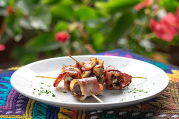 Photograph of informal food made from bacon, meat and cheese placed on a white plate with small herbs scattered with camera de-stressing with traditional tablecloth