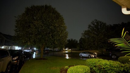 View from the front yard of the house at suburb street during the storm. Flashing lightening of thunderstorm light up the sky . Close up shot from inside the building