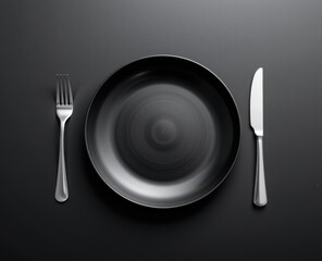 Minimalist black plate with silver cutlery on a dark surface.