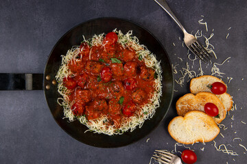 Spaghetti with meatballs and tomato sauce in a pan on a dark background
