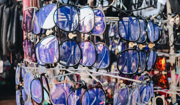 A closeup photo of various eyeglasses and sunglasses displayed on a rotating rack at a street market. The image shows different frame styles and colors