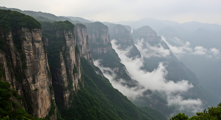 Dramatic panoramic view of towering cliffs shrouded in mist and lush green vegetation under a cloudy sky, showcasing a majestic natural landscape