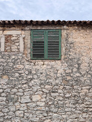 weathered wooden green shutters on window against stone wall with roof tiles on old house in Croatia