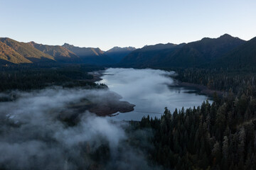 Aerial drone picture of sunrise at Wynoochee Lake dam in Olympic National Forest, Washington State, USA, showing calm water, low clouds, and forested mountain landscape in peaceful autumn morning	
