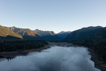 Aerial drone picture of sunrise at Wynoochee Lake dam in Olympic National Forest, Washington State, USA, showing calm water, low clouds, and forested mountain landscape in peaceful autumn morning	
