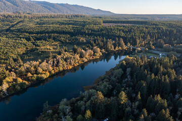 Aerial drone picture of Quinault Lake in Olympic National Park, Washington State, USA, showing golden autumn sunset light over calm blue water surrounded by evergreen forests, fall mountain landscape	