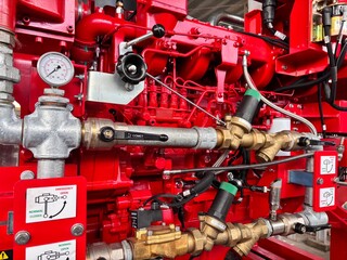 Close-up of a bright red industrial fire pump system with silver and brass piping, pressure gauges, and control valves, essential for fire suppression and safety.