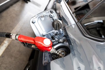 Fuel nozzle inserted in car gas tank as it's being refueled at gas station pump. Close up