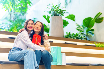 Happy Asian daughter give pink gift box to mother while shopping together at shopping mall. Senior mom and adult child girl celebration birthday party or mother's day. Happy Family relationship.
