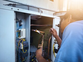 Refrigeration technician is welding industrial HVAC refrigerant pipes, industrial air conditioning repair concept.