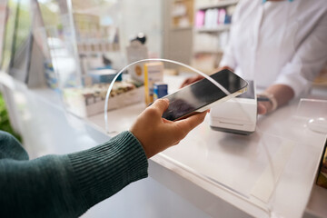 Close up of woman paying with smart phone in pharmacy.