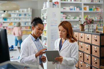 Female pharmacists using digital tablet while working in pharmacy.