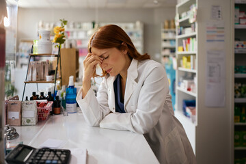 Exhausted pharmacist holding her head in pain while working in pharmacy.