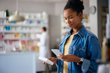 Smiling black woman using smart phone while buying medicine in pharmacy.