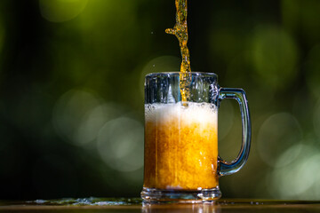 Golden craft beer poured on green outdoors. Lager beer with foam in glass mug. Beer splash on nature background. Pouring amber ale in nature. Brewed beer with bubbles and foam. Craft brewery lager.
