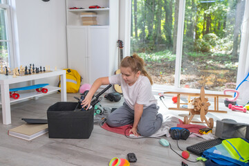 Child tidying scattered toys on the floor. Kid cleaning messy children room at home. Teen helping with household chores. Kid organizing toys in untidy playroom. Children cleaning up messy interior.