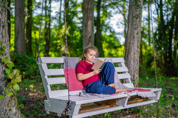 Fototapeta premium Child playing and dreaming on swing outside. Happy child enjoying playful activity in garden. Young kid sitting calmly on swing in nature. Child enjoying freedom and fun on backyard swing.
