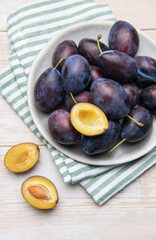 Fresh ripe plums in grey bowl on wood table