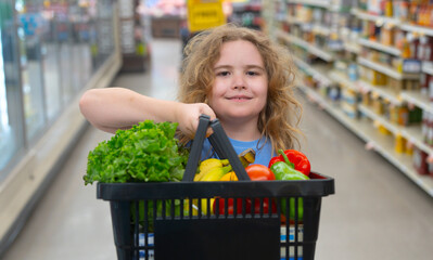 Child in grocery store. Child with shopping cart full of veggies. Kid choosing vegetables in grocery . Child shopping in grocery. Grocery shop fun for kids. Child in hypermarket.