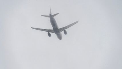 A plane is flying through a cloudy sky. The sky is overcast and the plane is low to the ground