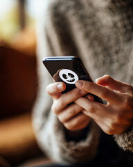 Close-up of hands holding smartphone with Halloween ghost sticker in warm indoor lighting
