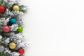 Colorful baubles with glitter and green artificial fir branches covered with hoarfrost and white snow. Light gray table background. Closeup. Christmas decoration. Empty place for text. Top down view.