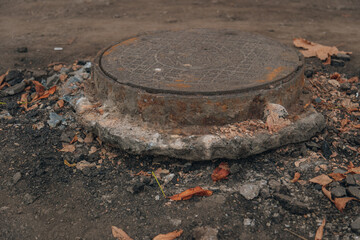 A close-up of an old, heavy cast-iron manhole cover perched on a pedestal of hardened mortar or...