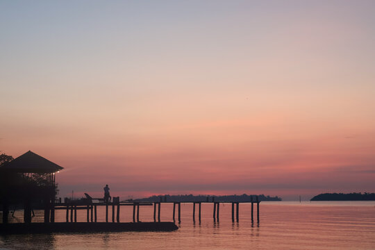 Simple, rustic wooden pier extending over the water at sunset, with calm water and soft twilight colors in the sky above the beach.