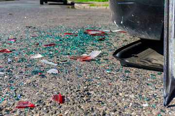Broken glass and plastic fragments after a car collision on a city street, close-up of asphalt and damaged bumper part of a passenger vehicle