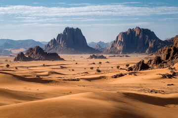 Naklejka premium Desert landscape, sand dunes and rocky mountains sunset. Dramatic view sahara. Red Mars like landscape. beautiful rock formations. Orange red sand desert, rocky formations and mountains background.