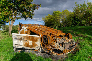 Burnt car after a road accident overturned on the roof, rusty wreck of a passenger vehicle on green...