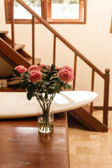 Pink chrysanthemums in a glass vase on a background of white surfboard. Flowers in the surfer living room. Bouquet of flowers in the interior of the house