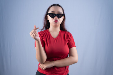 Fototapeta premium A woman in sunglasses and a red shirt makes a finger heart gesture with a pouting expression.