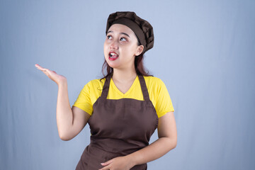 A woman in a chef's hat and apron looks up with a surprised expression and an open hand.