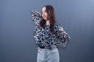 A woman in a floral blouse and jeans poses with one hand on her neck. She smiles slightly.