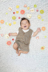 Fototapeta premium A baby is laying on a bed with a variety of fruits surrounding him. The baby is smiling and he is enjoying the fruits. Concept of happiness and playfulness