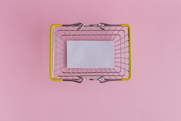 Shopping cart with a blank sheet of white paper inside on a pink background © Татьяна Зернова