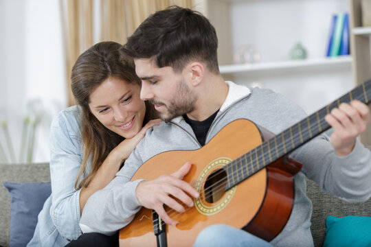 couple embracing on couch while man playing guitar at home - Powered by Adobe