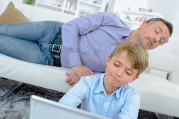 Man looking over shoulder of child using laptop