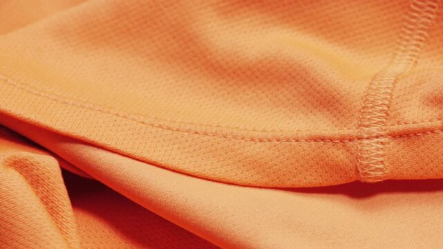 An orange polyester T-shirt shows mesh texture and a stitched seam as the camera pans slowly from left to right