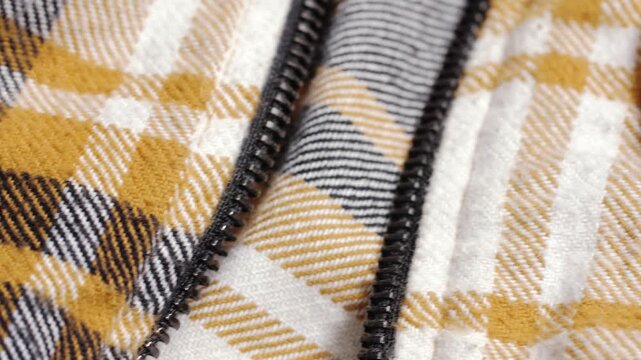 Mustard plaid flannel shows its brushed texture and zipper teeth as the camera pans slowly left to right