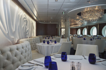 Formal and elegant ocean view a la carte dining room restaurant onboard luxury cruiseship cruise ship liner with set tables in white and blue Art Deco interior design style ceiling ambient lighting