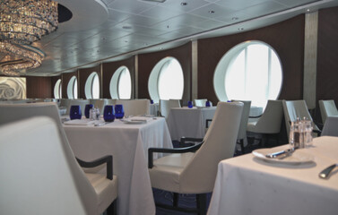 Formal and elegant ocean view a la carte dining room restaurant onboard luxury cruiseship cruise ship liner with set tables in white and blue Art Deco interior design style ceiling ambient lighting